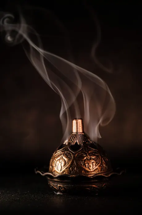 An engraved copper burner with bakhoor smoke rising from it