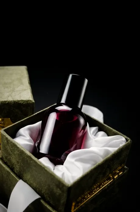 A dark perfume bottle on white silk inside a velvet gift box
