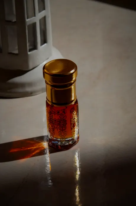 A small bottle of oud oil with a gold cap on marble in afternoon light