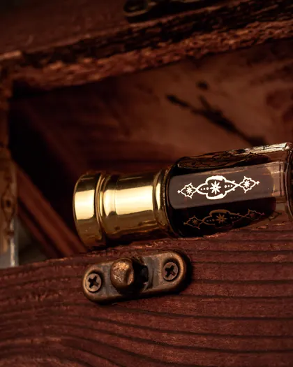 A black oud oil bottle with a gold cap inside a wooden box