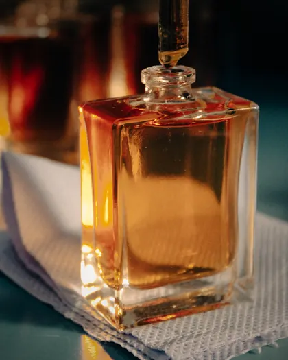 A pipette filling an amber perfume bottle