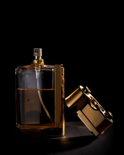 A perfume bottle with its gold cap off, against a dark background