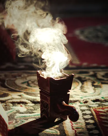 A wooden mabkhara on a rug, with thick smoke rising