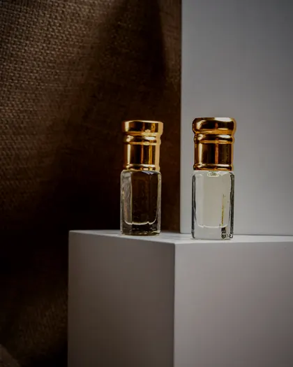 Two musk oil bottles with gold caps on a white plinth